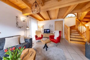 A spacious living room with a wooden ceiling, a sofa, a red chair, a coffee table, and a TV. - Authentic Mountain Retreat for 12 (Wald im Pinzgau)