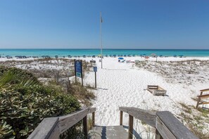 A beach with a wooden walkway leading to the shore, surrounded by sand and sparse vegetation.
