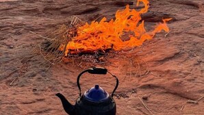 Una tetera negra sobre una superficie rocosa, con un fuego ardiendo cerca.