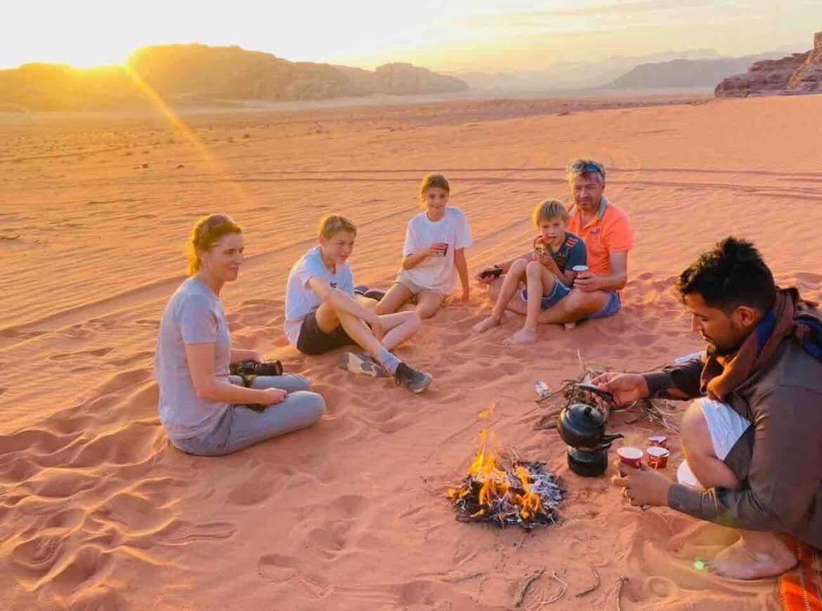 A group of people sitting on the sand around a campfire in a desert setting.