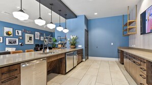 A modern kitchen with a central island, pendant lighting, and a blue accent wall. - The Melanie 1st Floor Condo with Pool & Gym Access (Tuscaloosa)