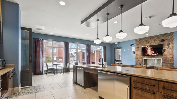 A modern kitchen with a large island, pendant lights, and a stone backsplash. - The Melanie 1st Floor Condo with Pool & Gym Access (Tuscaloosa)