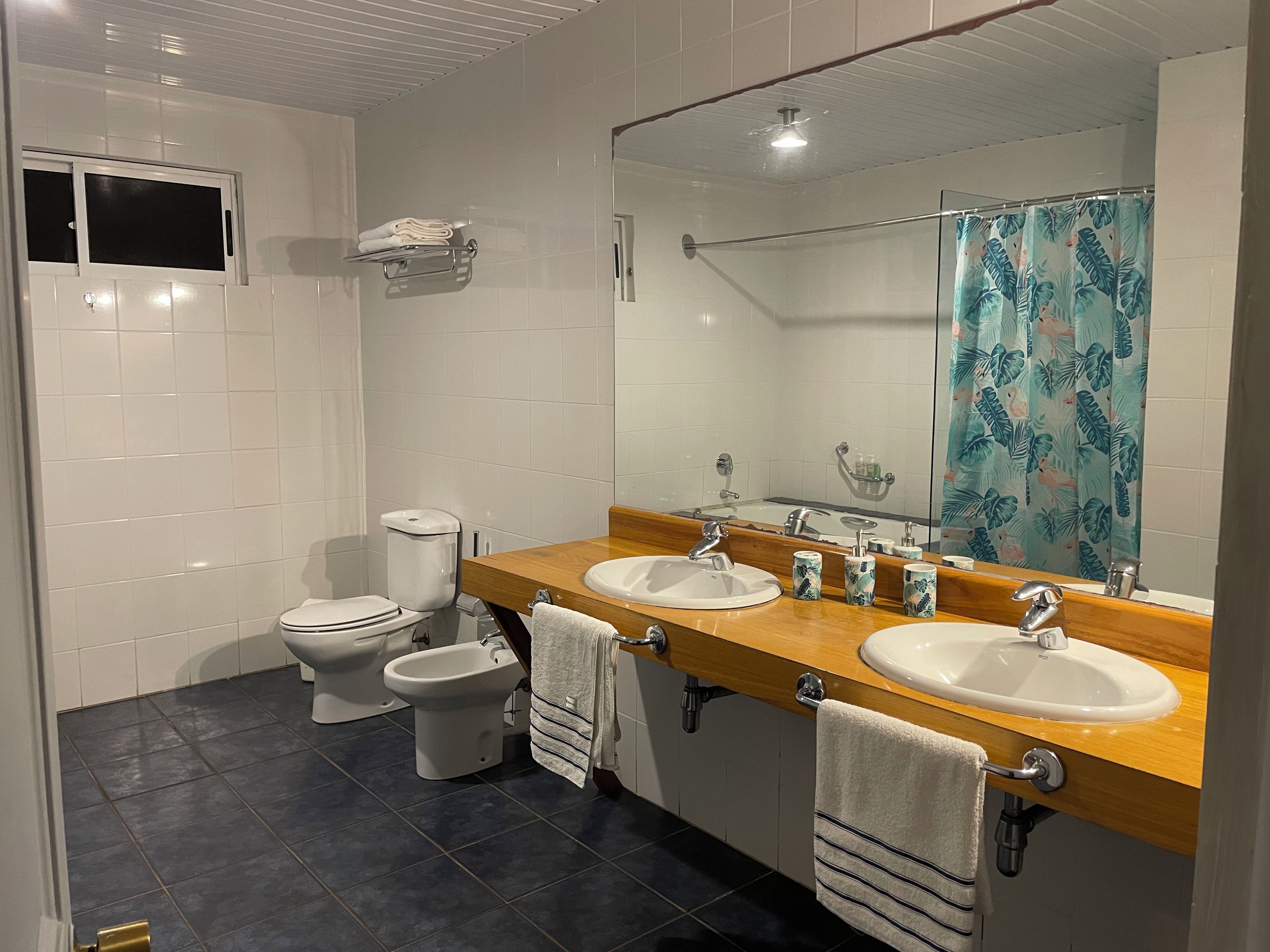 Un baño con dos inodoros, un bidé, un espejo grande y una ducha con cortina decorada con motivos florales.