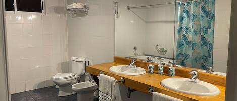 Un baño con dos inodoros, un bidé, un espejo grande y una ducha con cortina decorada con motivos florales.