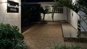 Una casa moderna con un cartel que dice "Manureva Nui" y un patio bien iluminado con plantas y piso de baldosas.