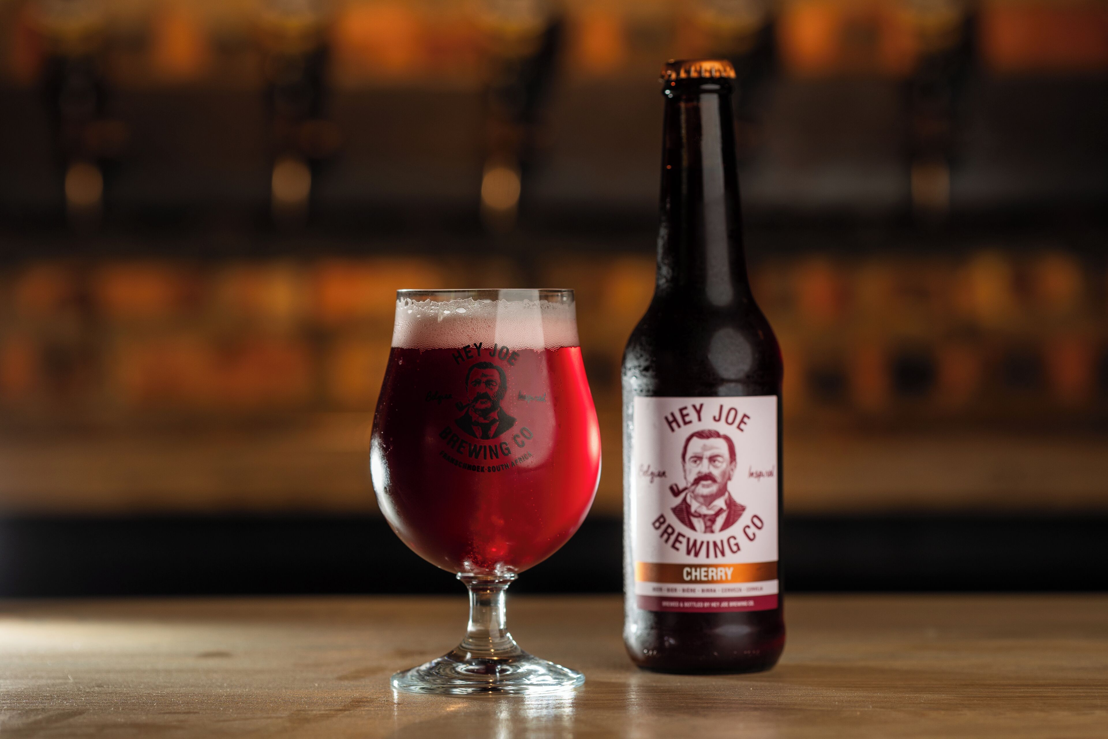 A glass of beer and a bottle labeled "Hey Joe Brewing Co." on a wooden surface.
