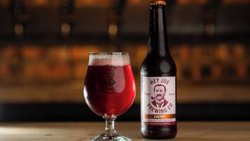 A glass of beer and a bottle labeled "Hey Joe Brewing Co." on a wooden surface.