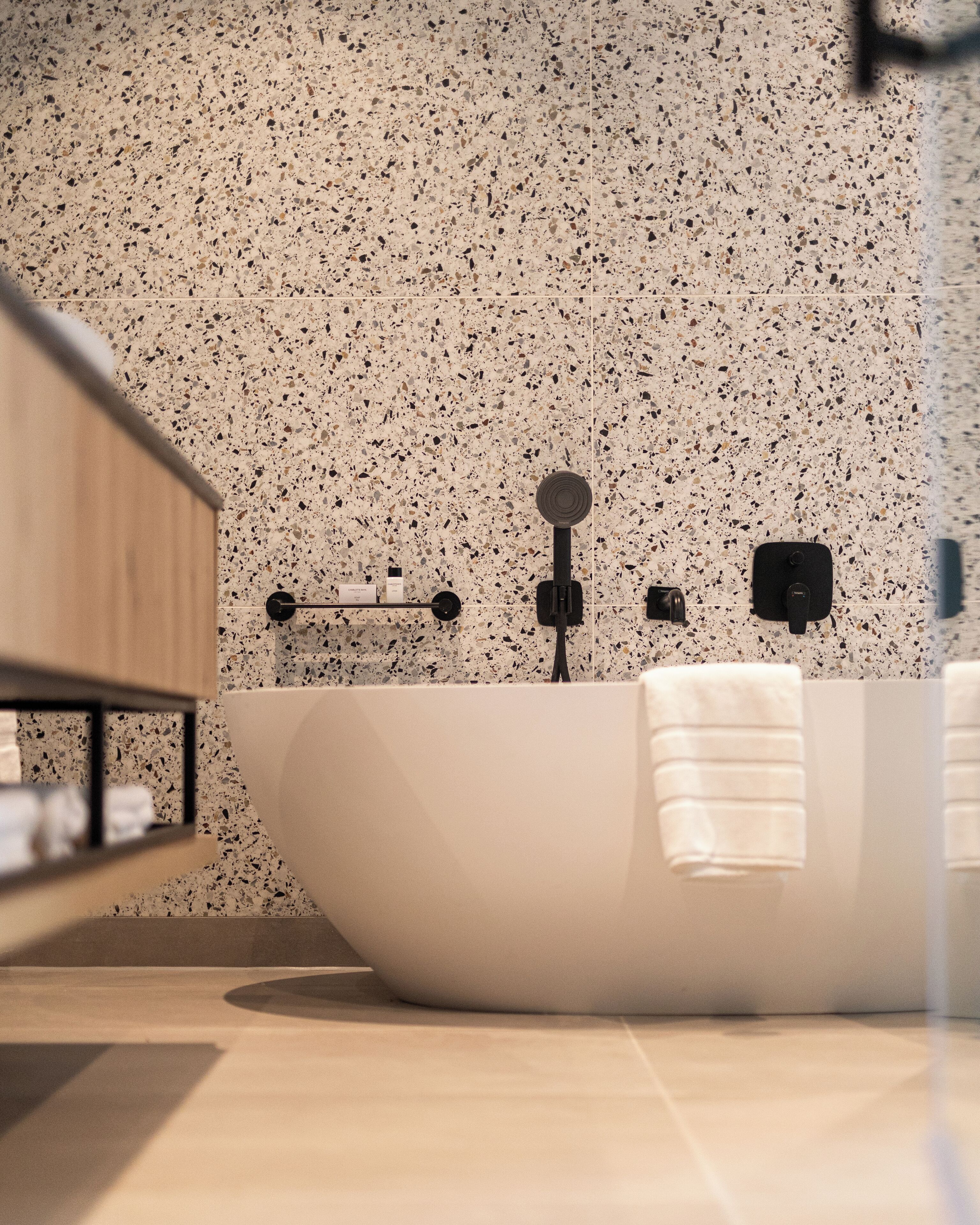 A modern bathroom with a freestanding bathtub, a wooden vanity, and a speckled backsplash.