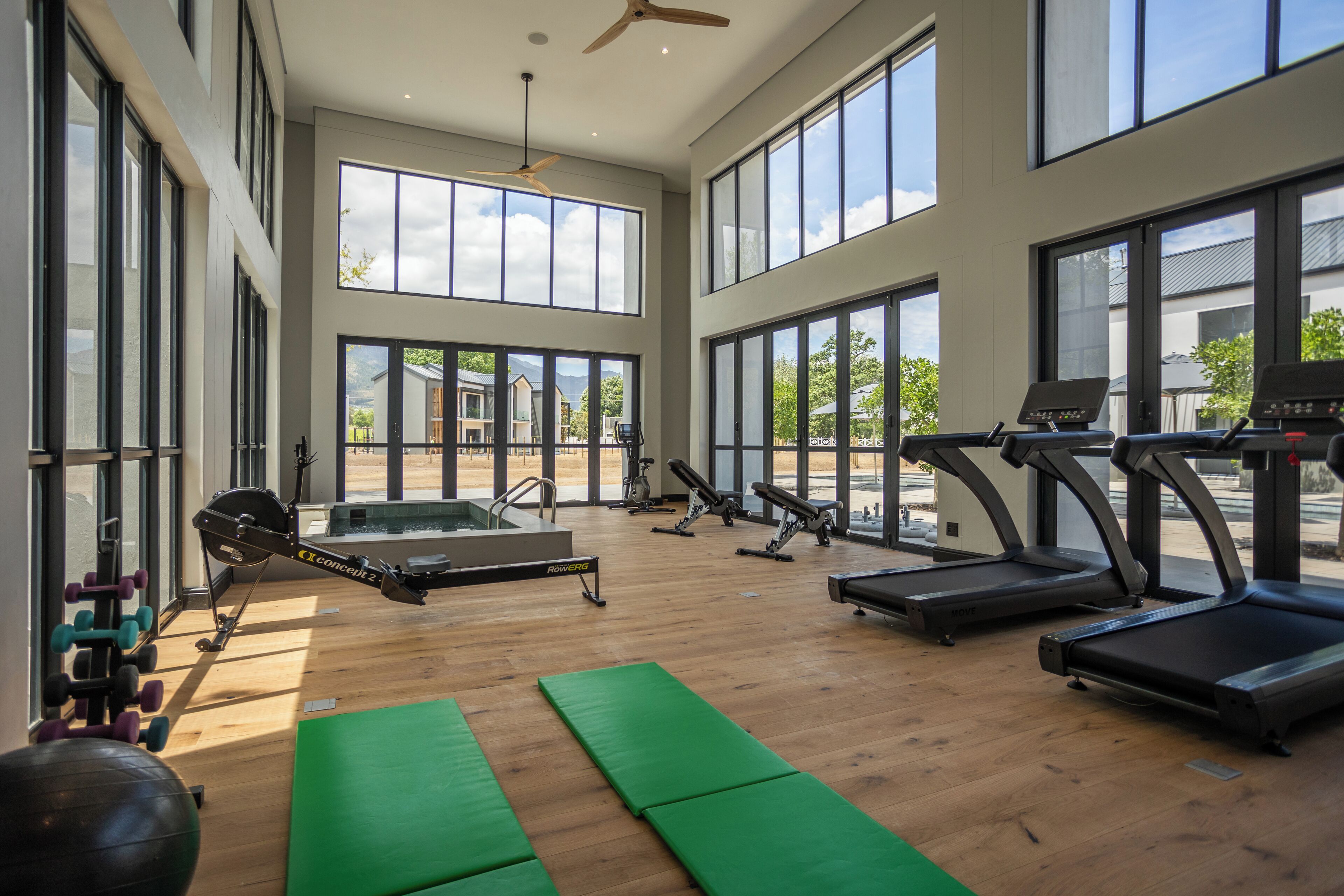 A spacious gym with large windows, treadmills, and various exercise equipment.