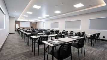 A conference room with rows of tables and chairs, a projector screen, and a whiteboard.