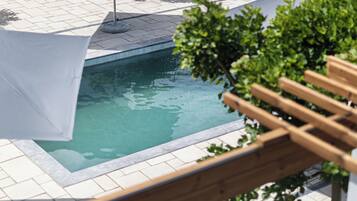 Un espace piscine doté d’une terrasse carrelée, d’un banc en bois et d’un auvent blanc.