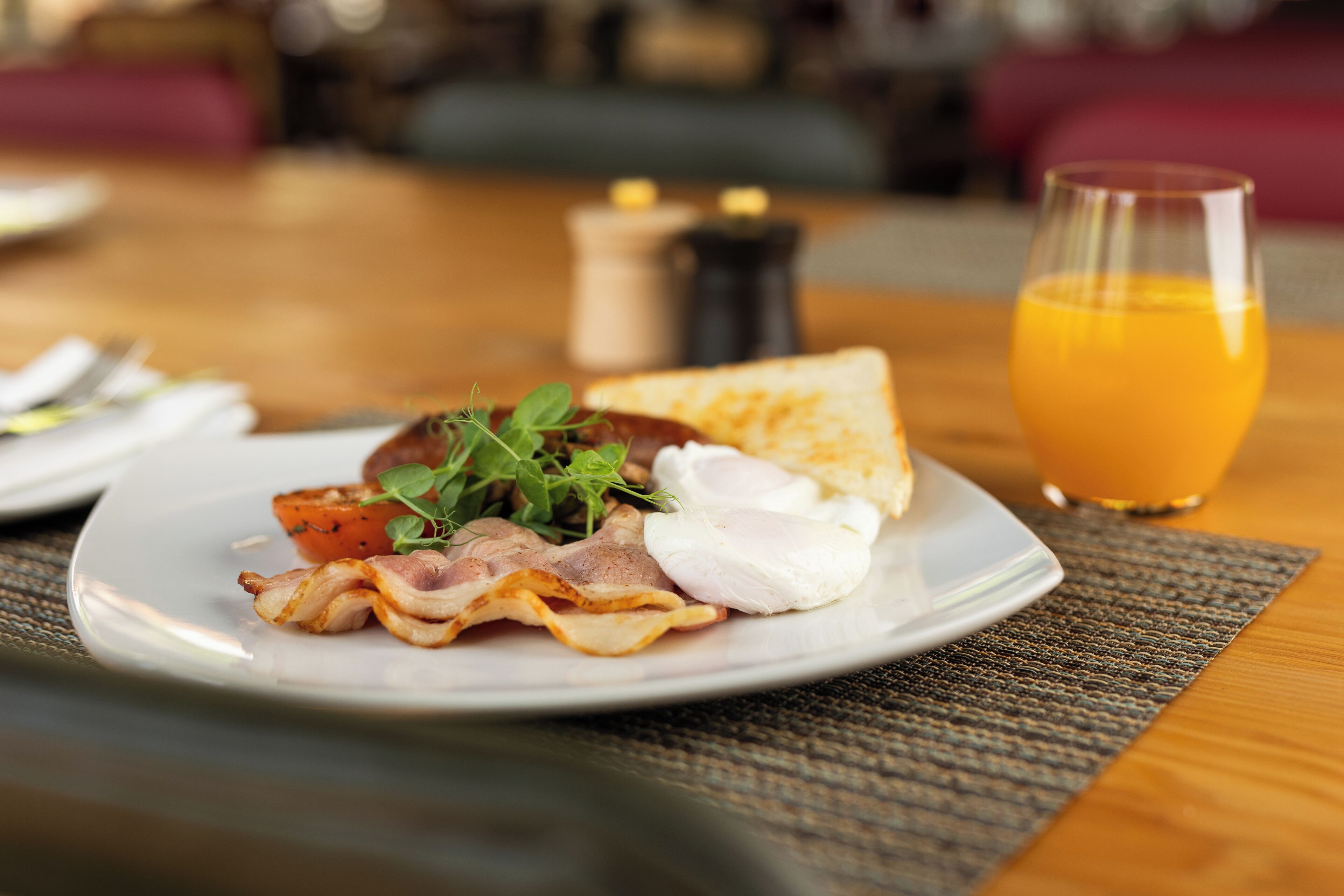 A breakfast plate with bacon, eggs, and toast, accompanied by a glass of orange juice, on a wooden table.