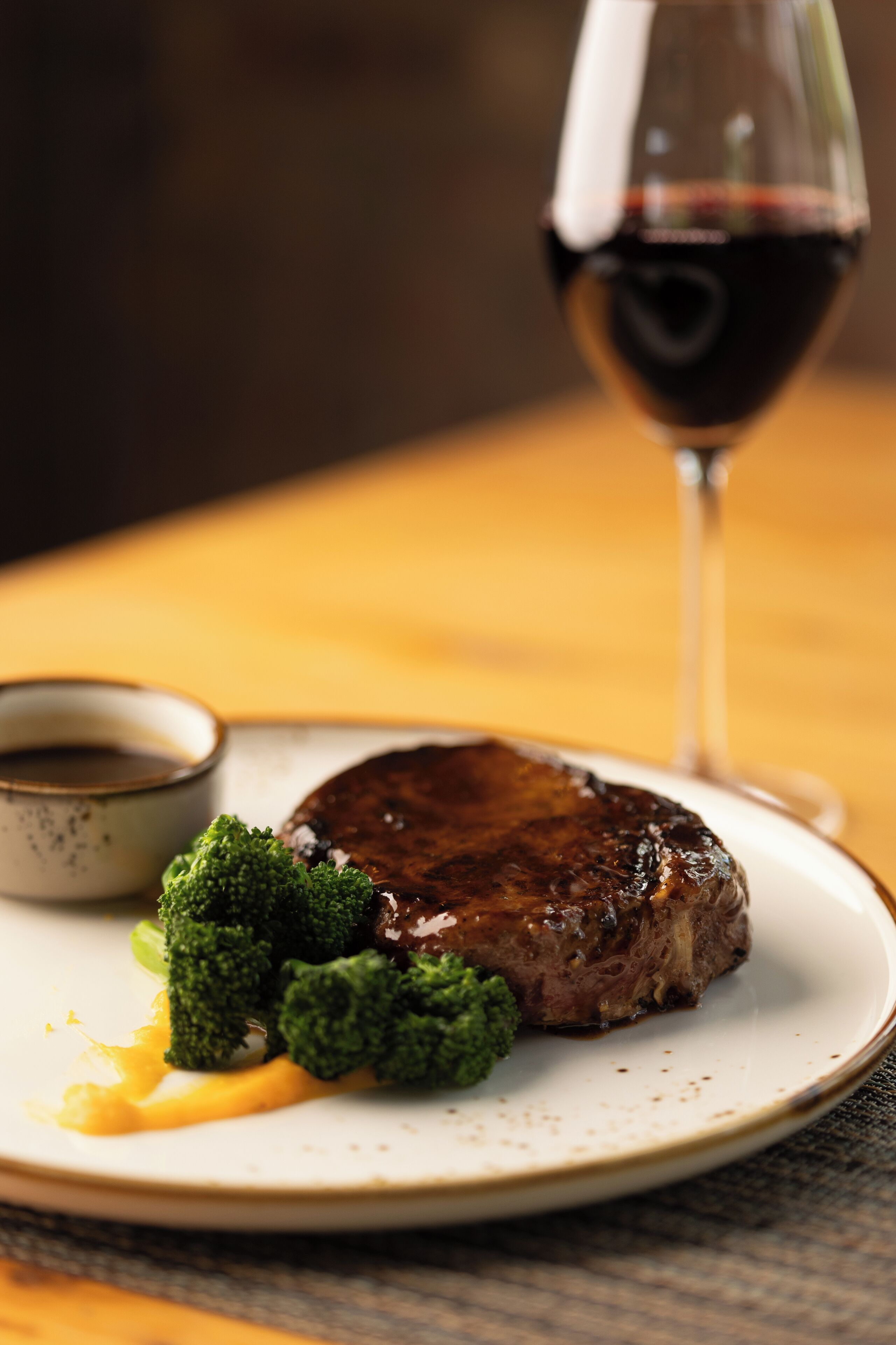 A plate with steak, broccoli, and a glass of red wine.