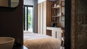 A modern hotel room with a large bed, a wooden vanity, and a view of the outdoors.