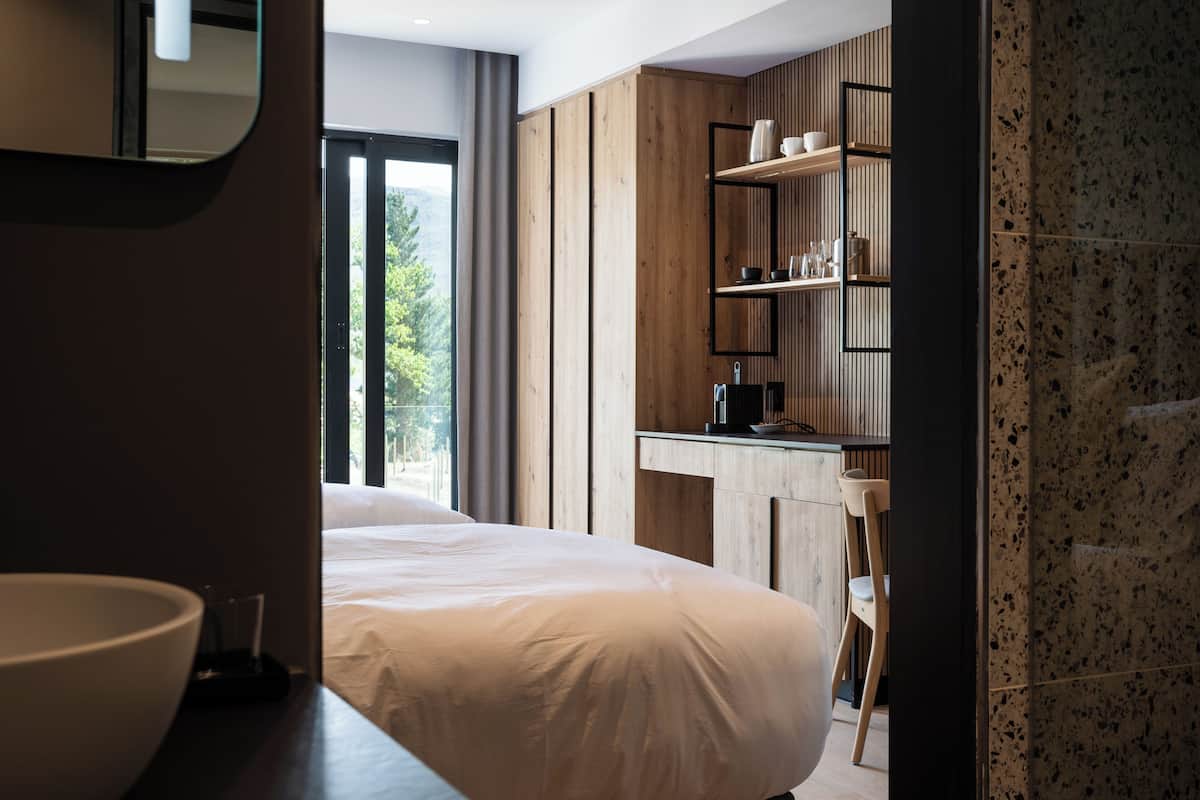 Ein modernes Hotelzimmer mit einem großen Bett, einem Holzinlay und Blick ins Freie.