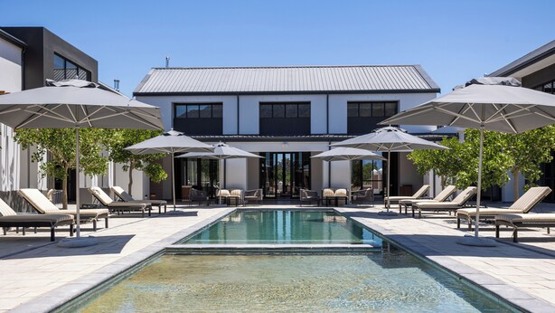 A modern outdoor pool area with lounge chairs and umbrellas, surrounded by a building with a metal roof.