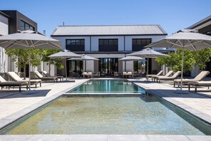 A modern outdoor pool area with lounge chairs and umbrellas, surrounded by a building with a metal roof. - @Franschhoek Hotel (Franschhoek)