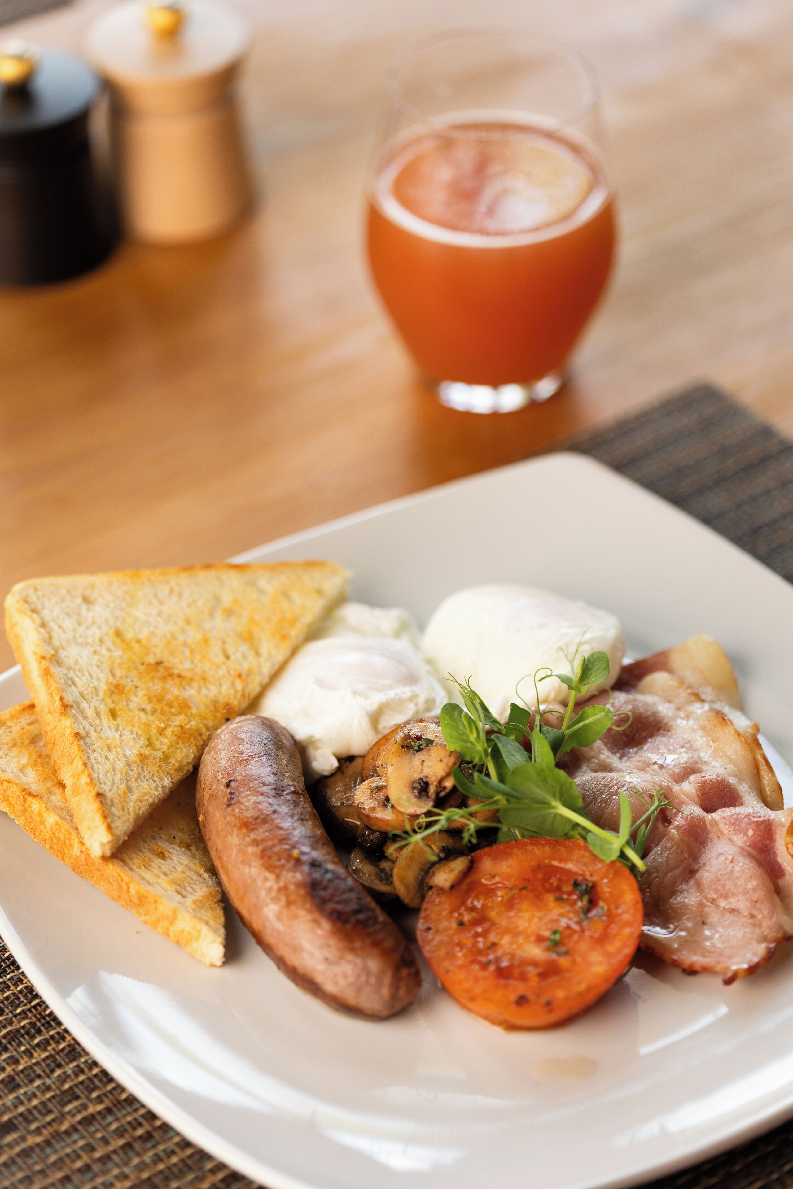 Un plato de desayuno con tostadas, salchicha, huevos, tocino y una rodaja de tomate.