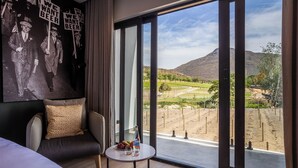 A hotel room with a large window, a bed, a sofa, and a small table with a bottle and glasses.