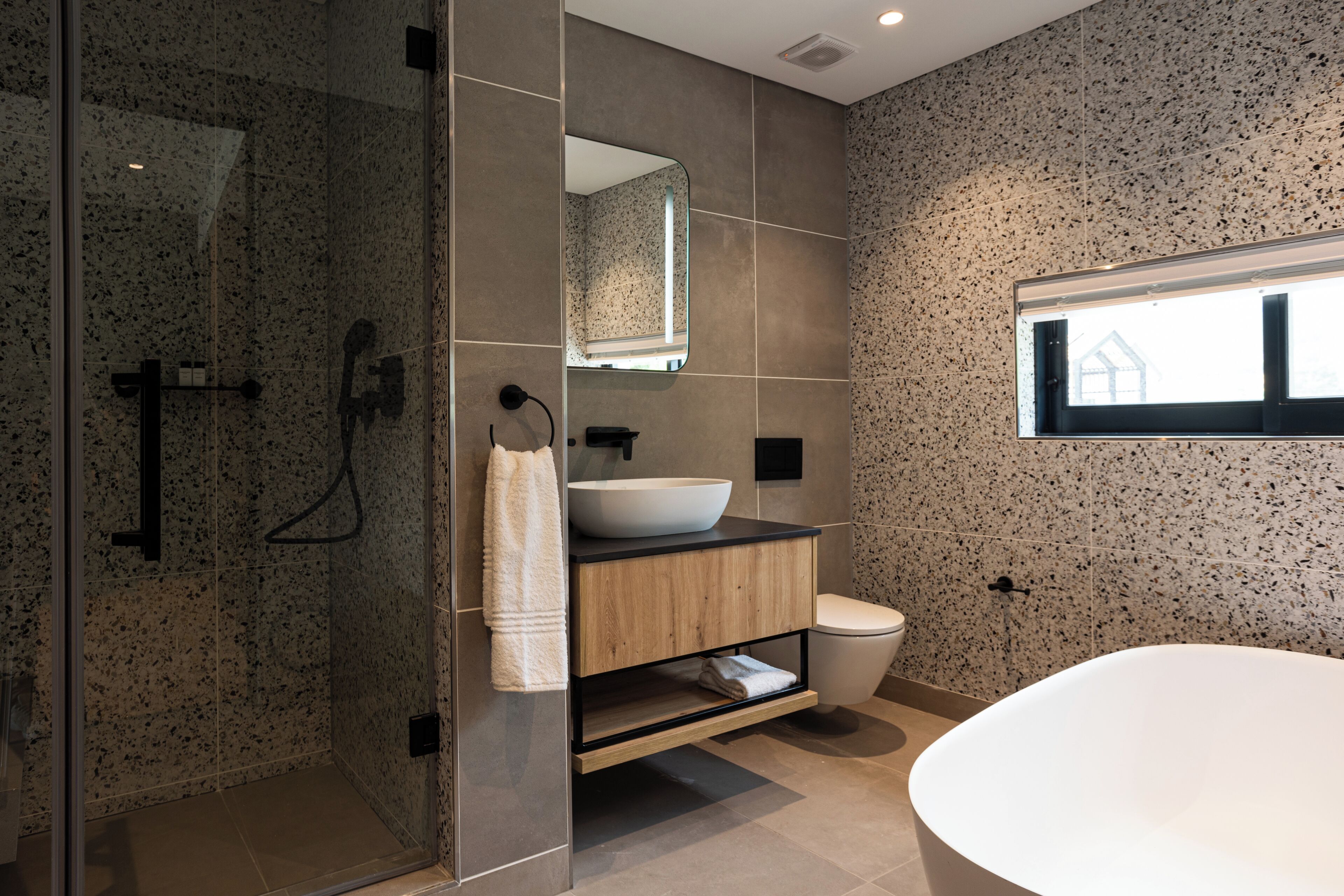 A modern bathroom with a glass-enclosed shower, a wooden vanity with a large sink, and a freestanding bathtub.