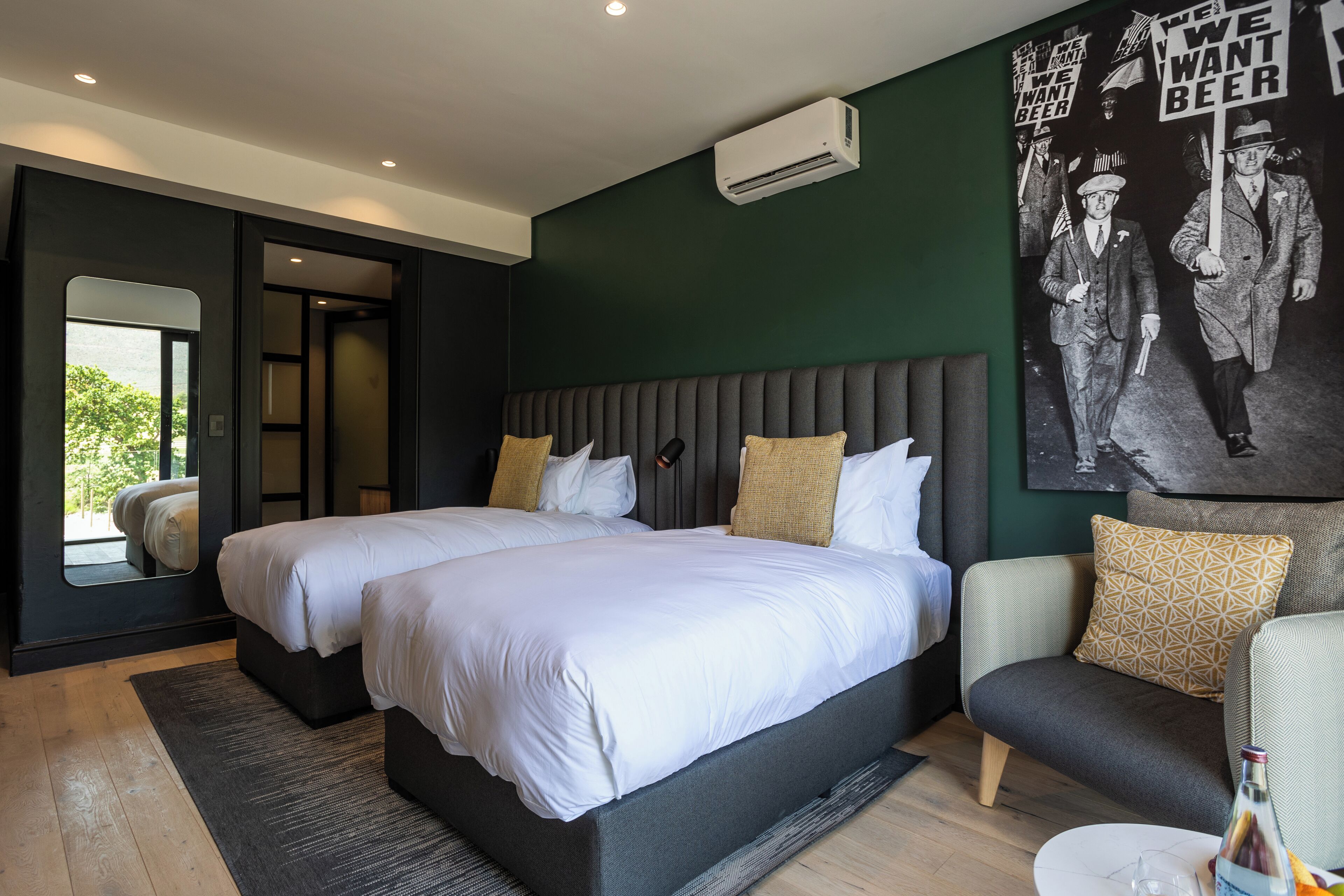 Une chambre d’hôtel moderne avec deux lits, un canapé, une table basse et une grande fresque murale.