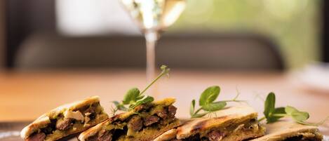 A plate with a sandwich cut in half, garnished with a sprig of herb, and a glass of white wine in the background.