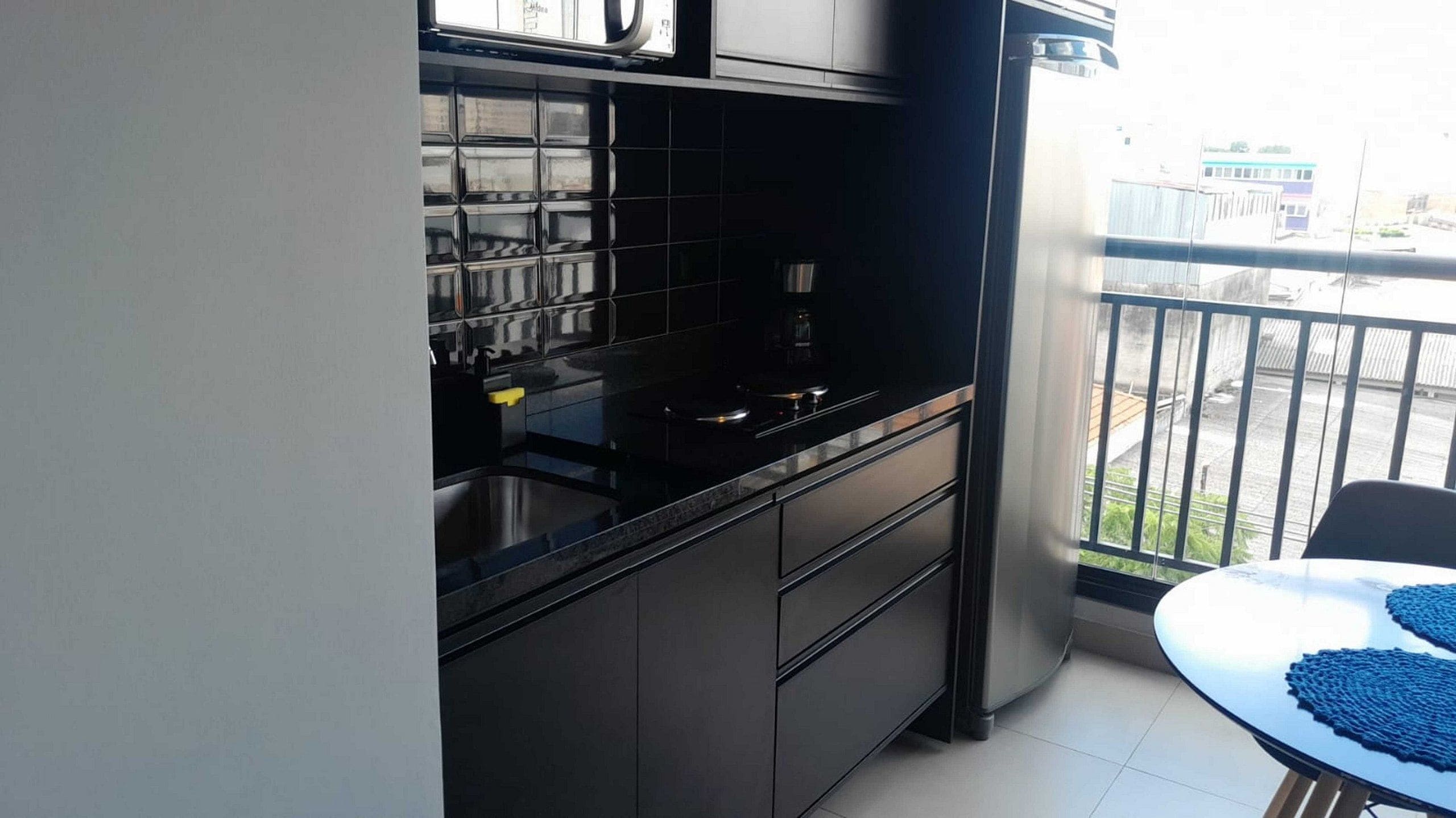 Cocina compacta con muebles negros, un lavamanos de acero inoxidable y una cafetera.