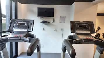 Una palestra con due tapis roulant, una TV montata a muro e un piccolo ripiano con un telecomando.