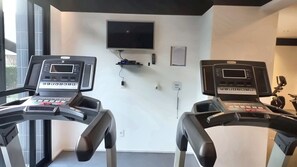 A gym with two treadmills, a TV mounted on the wall, and a small shelf with a remote control. - Elegance Suítes Anhembi (São Paulo)