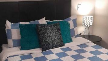 Un letto rifatto con una coperta a quadri, una testiera e una ventola a parete.