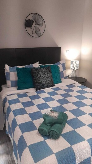A neatly made bed with a checkered bedspread, a headboard, and a wall-mounted fan. - Elegance Suítes Anhembi (São Paulo)