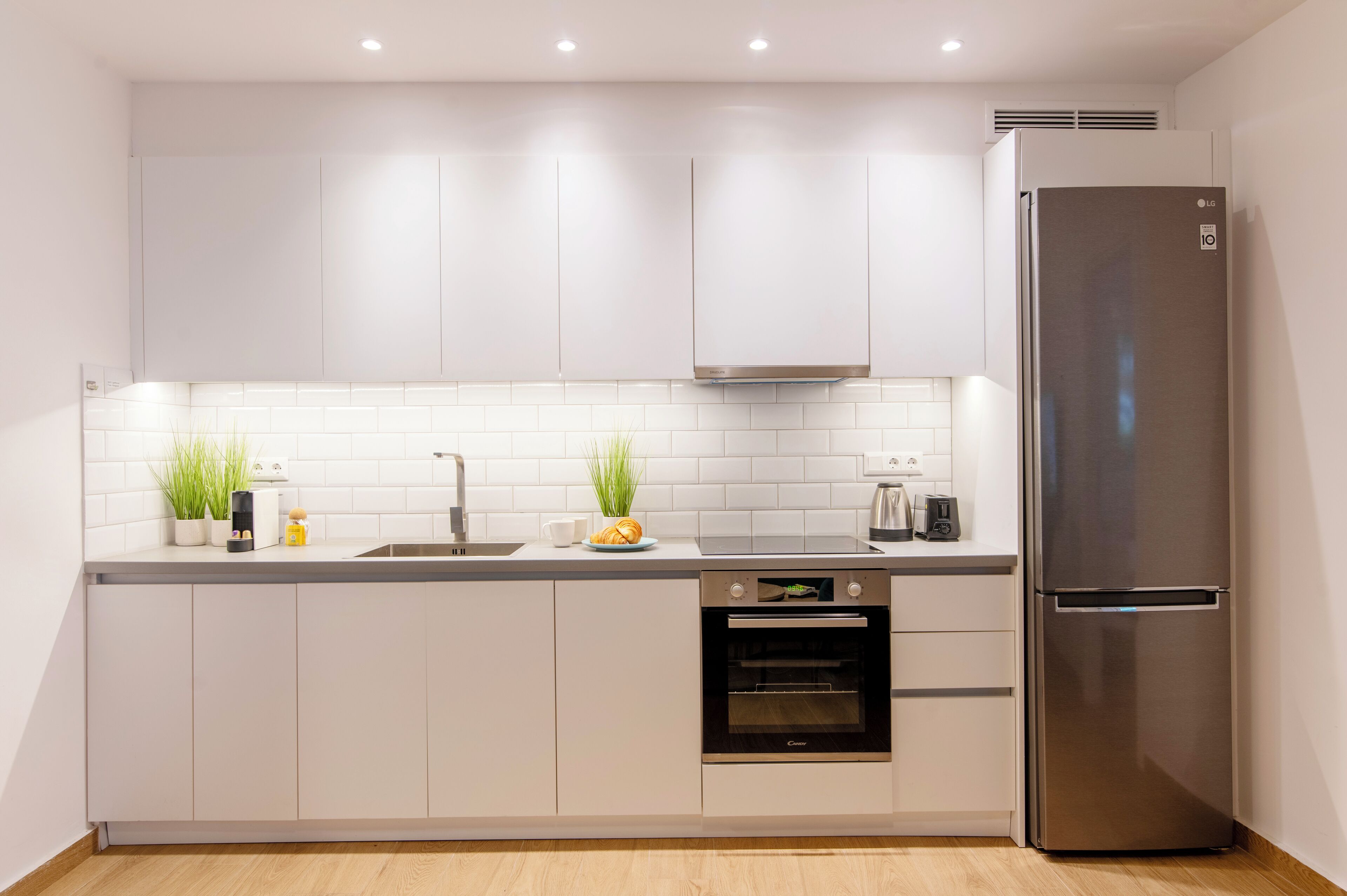 A modern kitchen with white cabinets, a stainless steel refrigerator, an oven, and a sink.