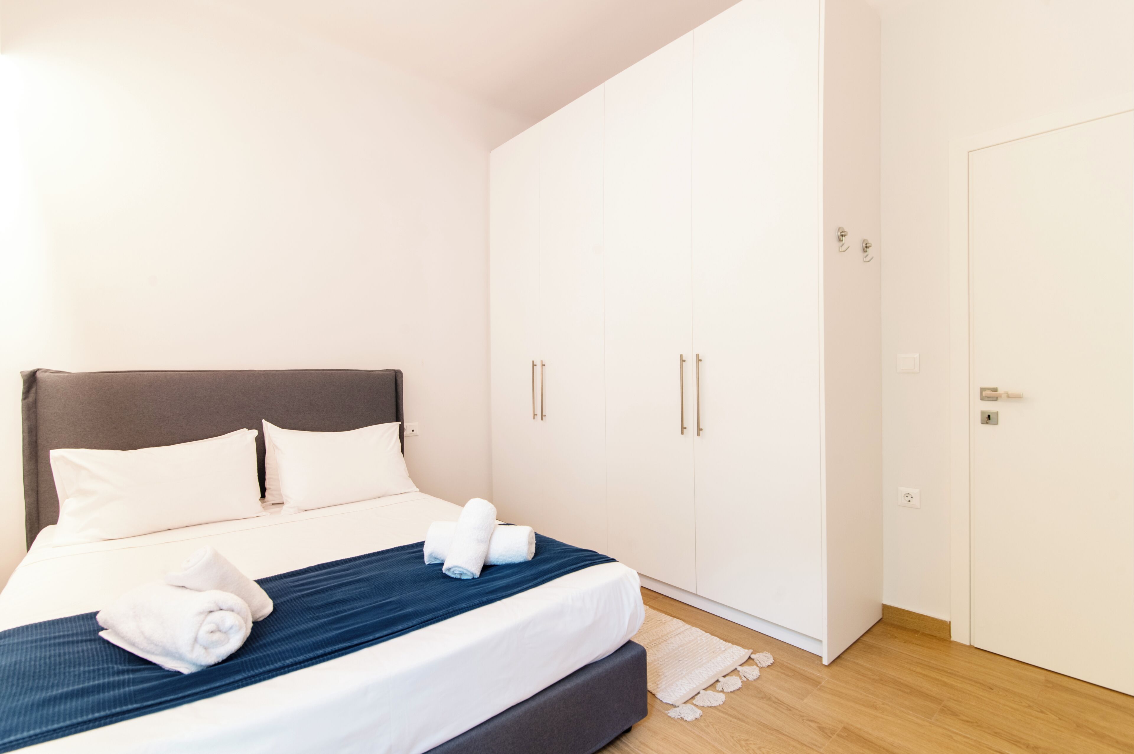 A neatly made bed with white and blue bedding, a grey headboard, and a white wardrobe with two doors.