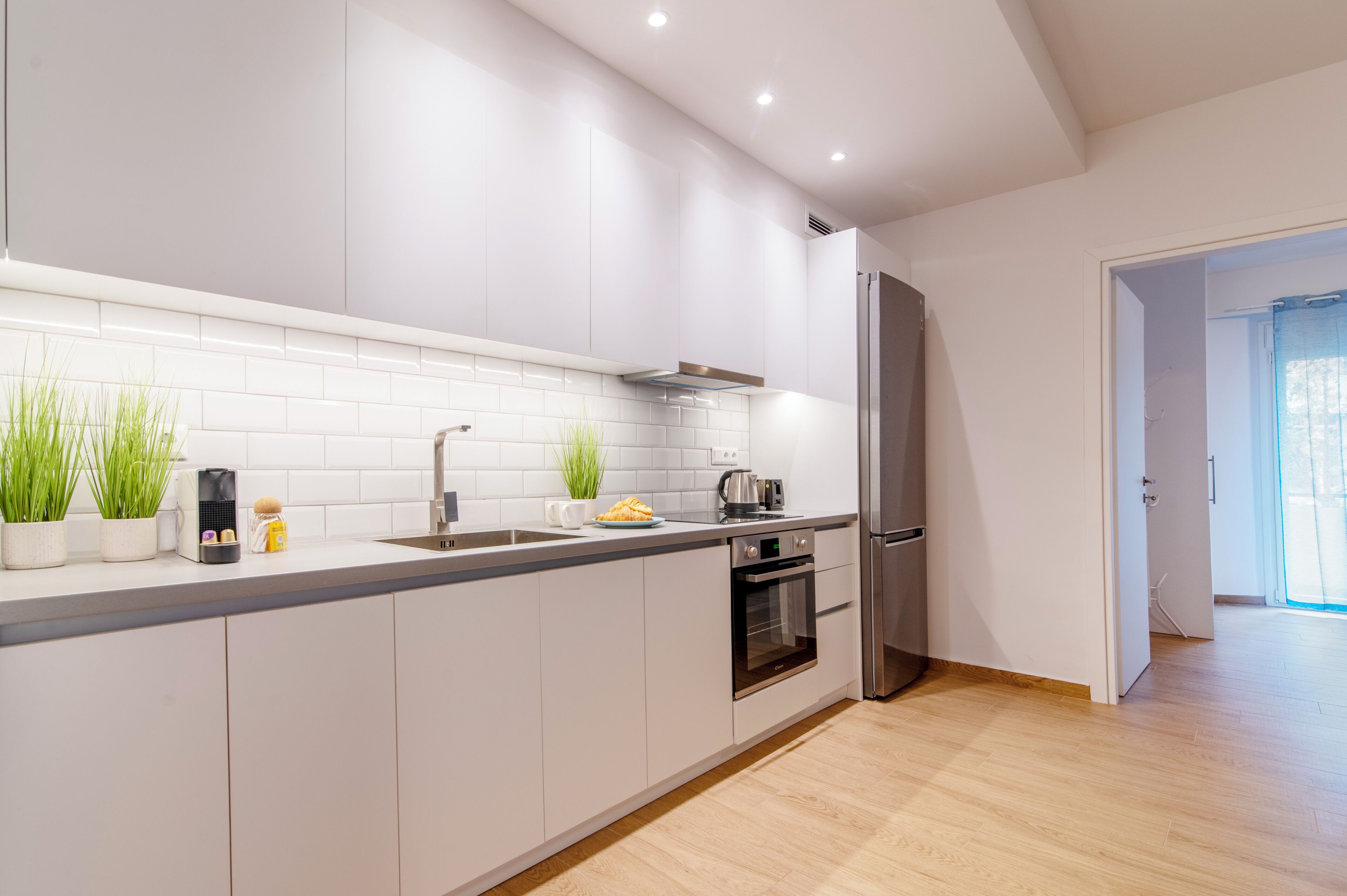 Une cuisine moderne avec des armoires blanches, un réfrigérateur en acier inoxydable et un plancher en bois.