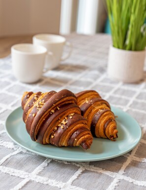 Two chocolate croissants on a light blue plate, with a white tablecloth and a potted plant in the background.