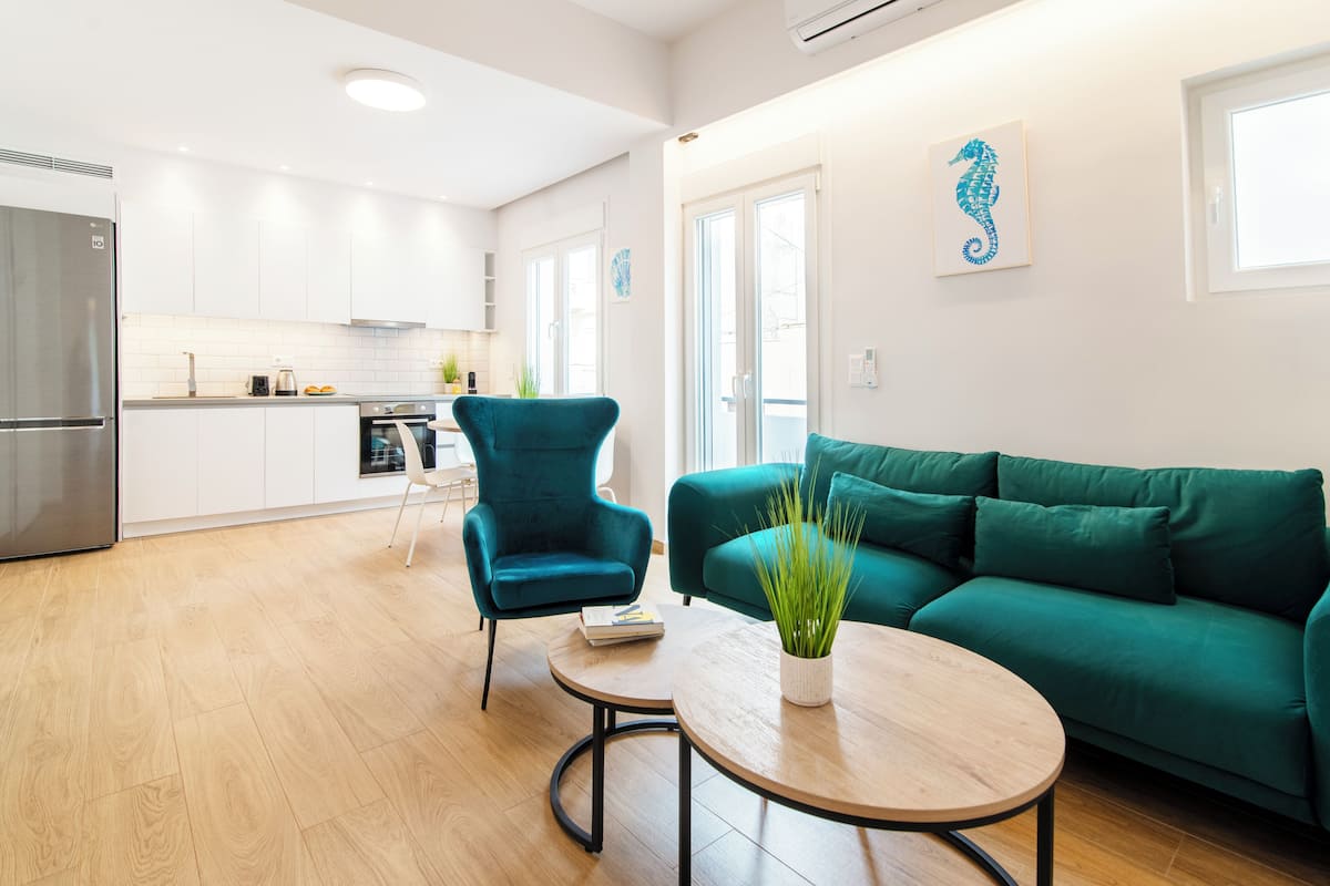 A modern living room with a green sofa, a teal armchair, and a round table with a plant.