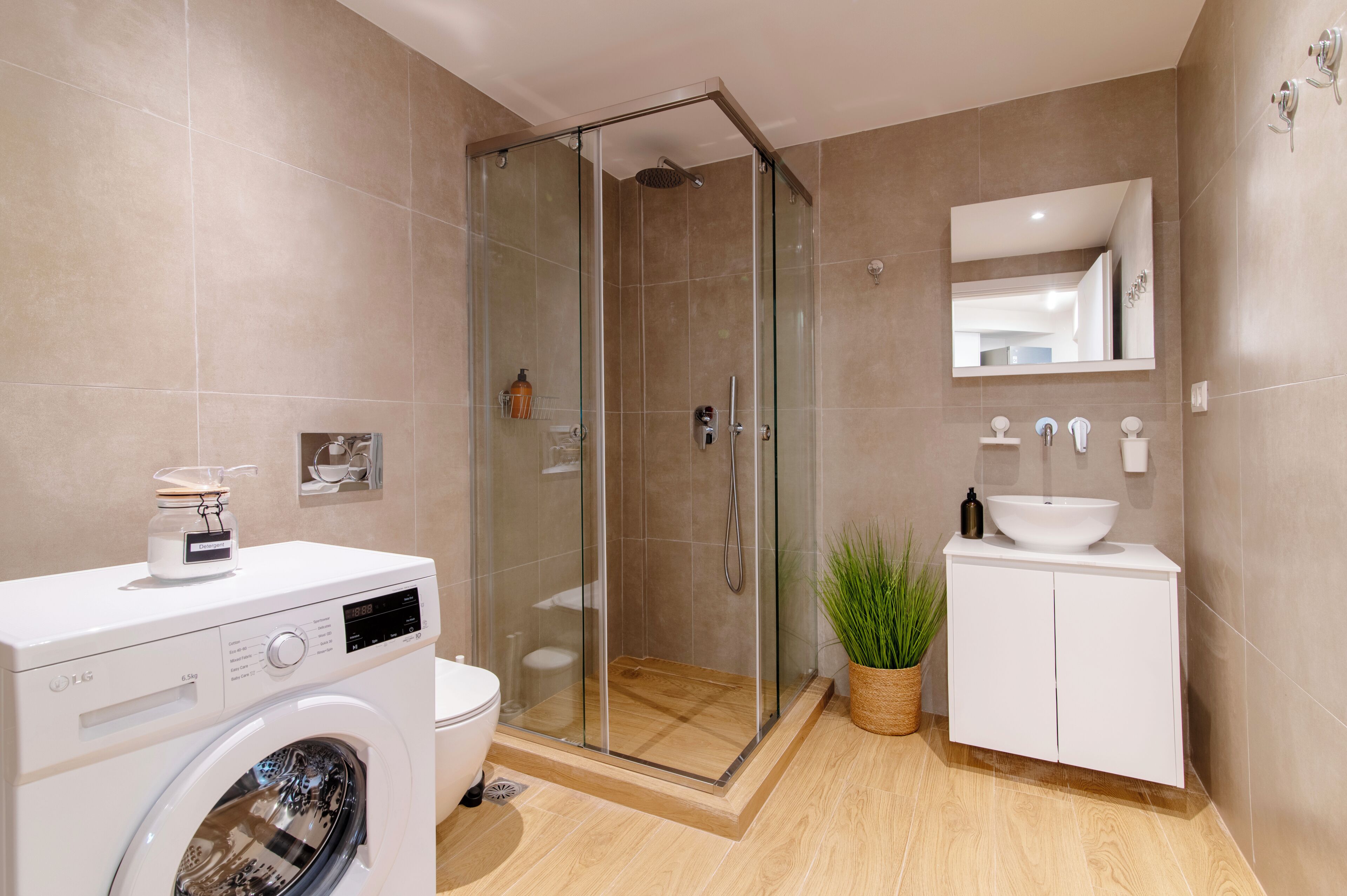 A modern bathroom with a glass-enclosed shower, a washing machine, a sink, and a mirror.
