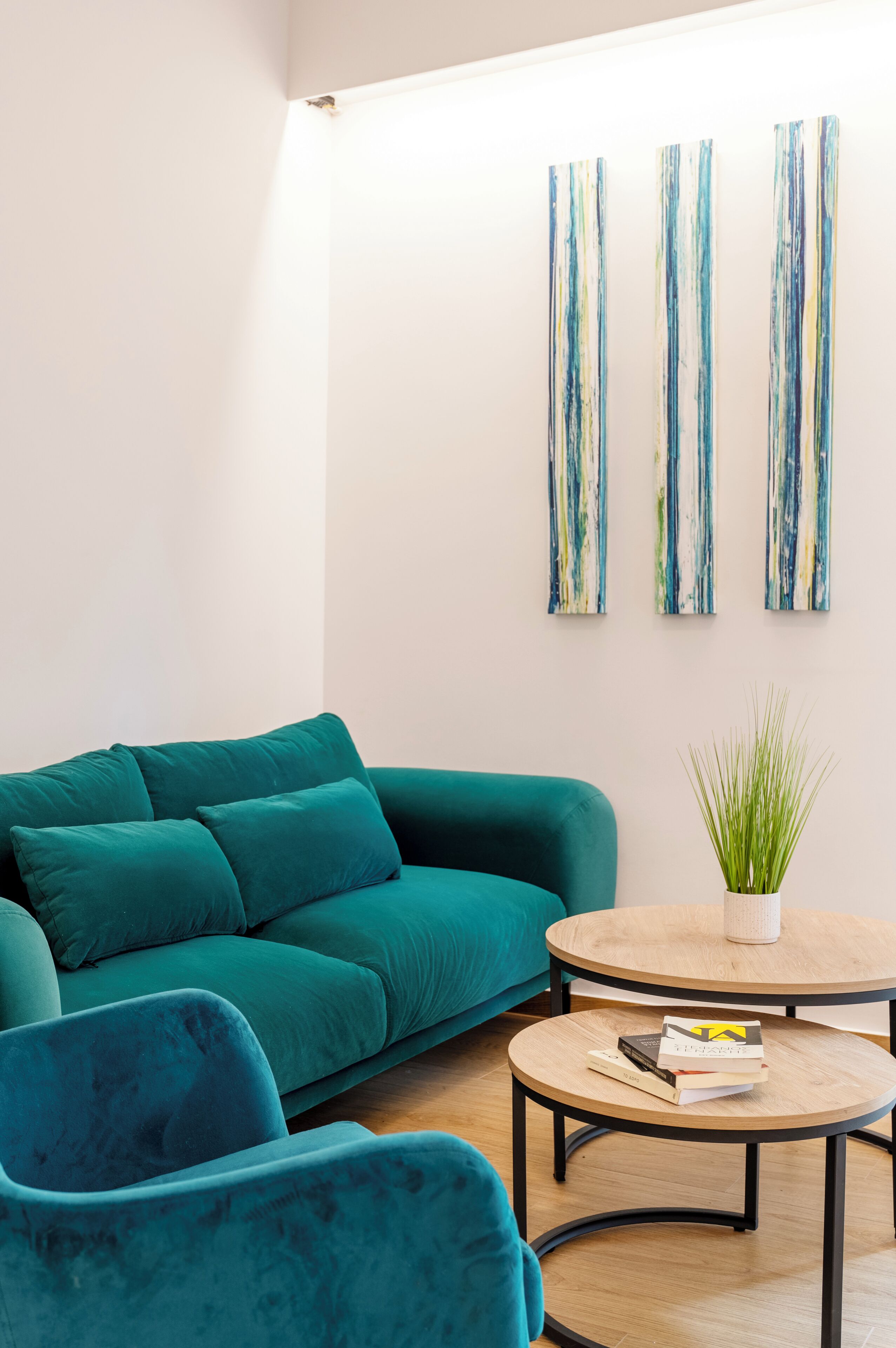A teal sofa, a round coffee table with books, and abstract wall art in a modern room.
