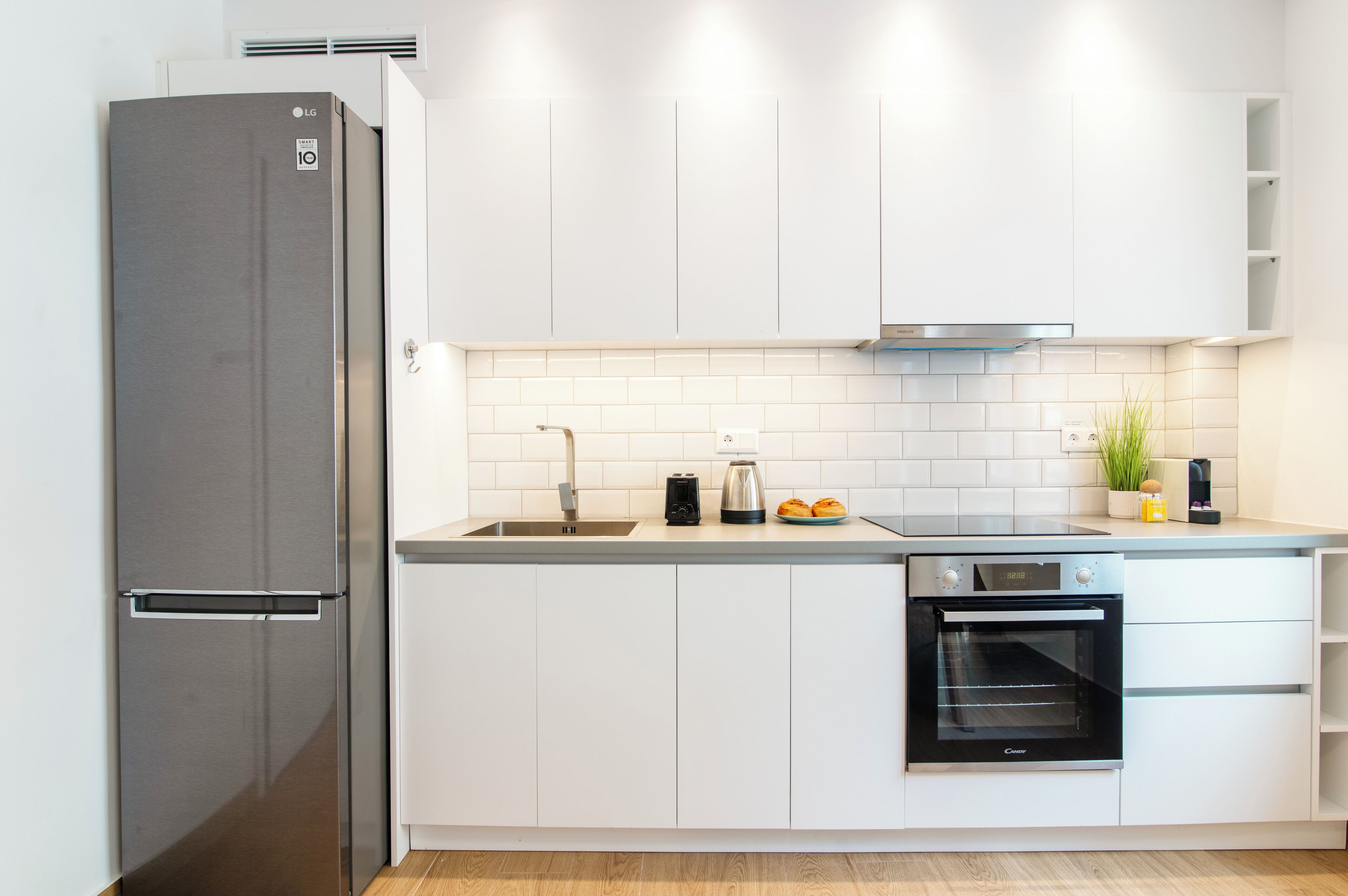 Una cocina moderna con armarios blancos, un refrigerador de acero inoxidable, un horno empotrado y un lavaplatos.