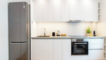 Una cocina moderna con armarios blancos, un refrigerador de acero inoxidable, un horno empotrado y un lavaplatos.