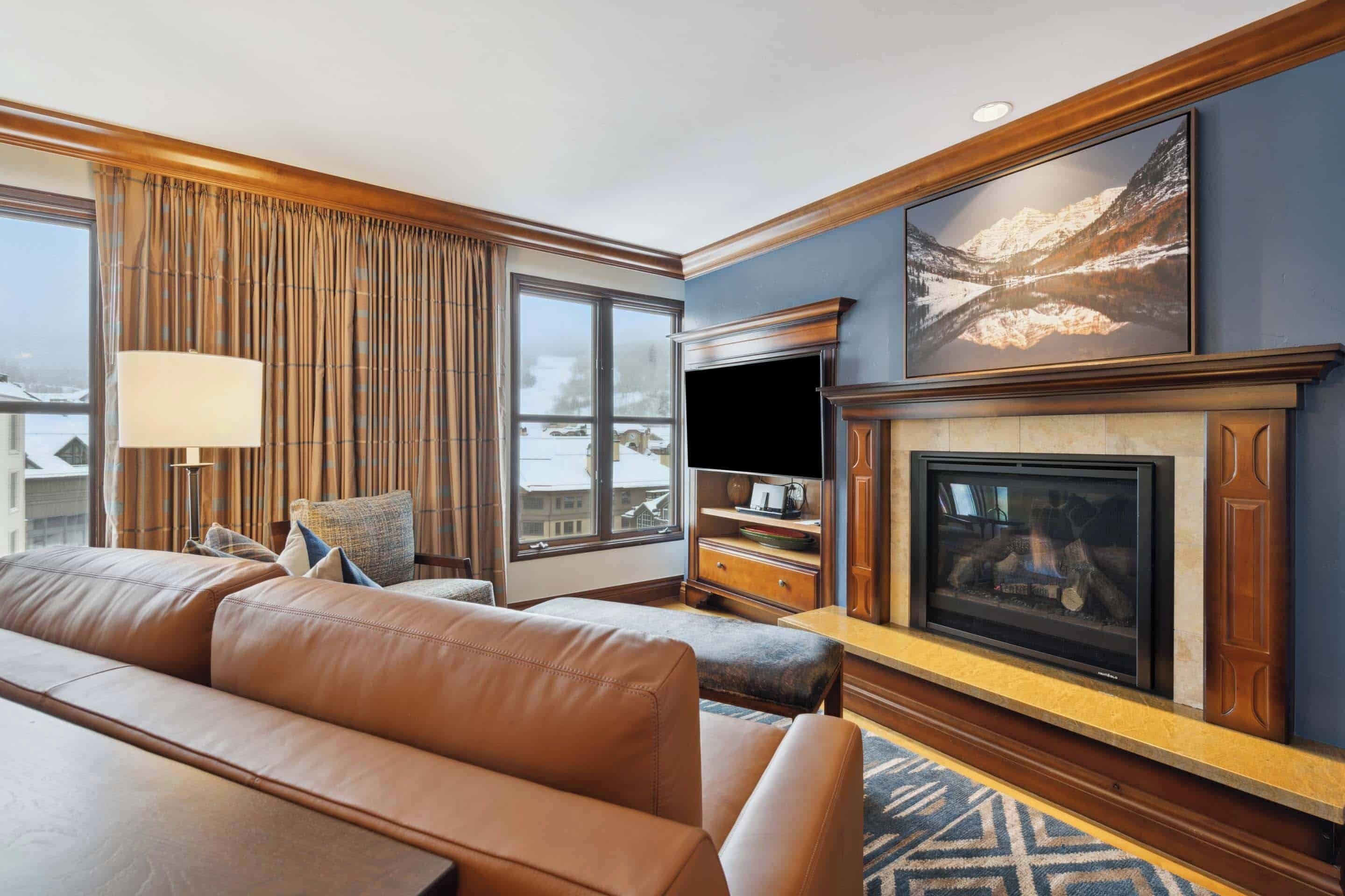 Ein Hotelzimmer mit einer großen Ledersofa, einem Flachbildfernseher, einem Kamin und einem großen Fenster mit Vorhängen.