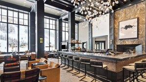 A spacious bar area with high stools and a long counter, large windows offering a view of a snowy landscape, and a fireplace with a modern design. - Hyatt Residence 4051 - 2 Bedroom Residence (Beaver Creek)