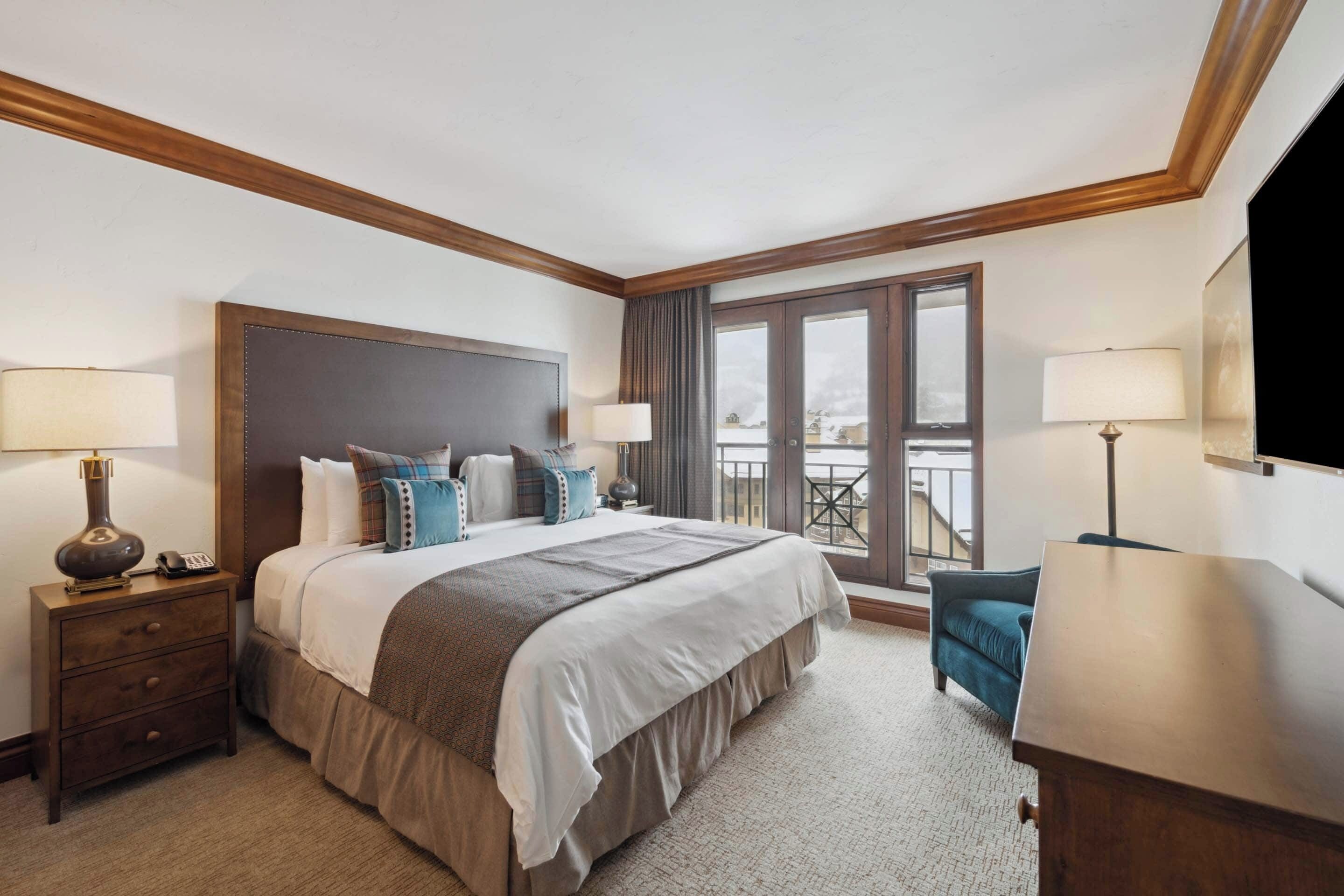 Une chambre d’hôtel avec un grand lit, une table de chevet avec une lampe, un bureau avec une lampe et un balcon avec vue.