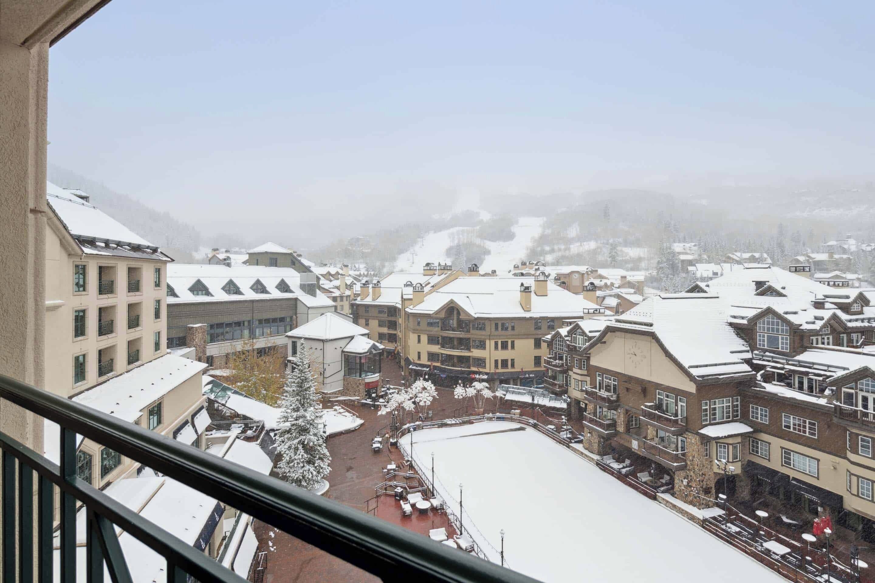 A snow-covered town with buildings, a central square, and a view of distant mountains.