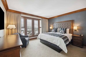 A hotel room with a large bed, a desk, a chair, and a view of the outdoors through a large window.
