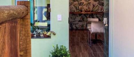 Puerta de vidrio que da a un comedor con papel tapiz tropical, una planta pequeña en maceta y un banco de madera en el exterior.