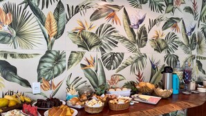 A buffet table with various food items and a tropical-themed wall in the background. - Pousada Cardeal Mota (Santana do Riacho)