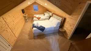 Un dormitorio acogedor en el ático con dos camas, una mesita y un ventanal.