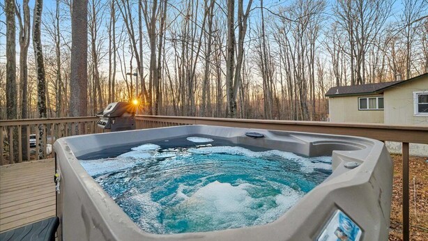 Un jacuzzi en una terraza de madera con vistas a árboles sin hojas y una casa al fondo.