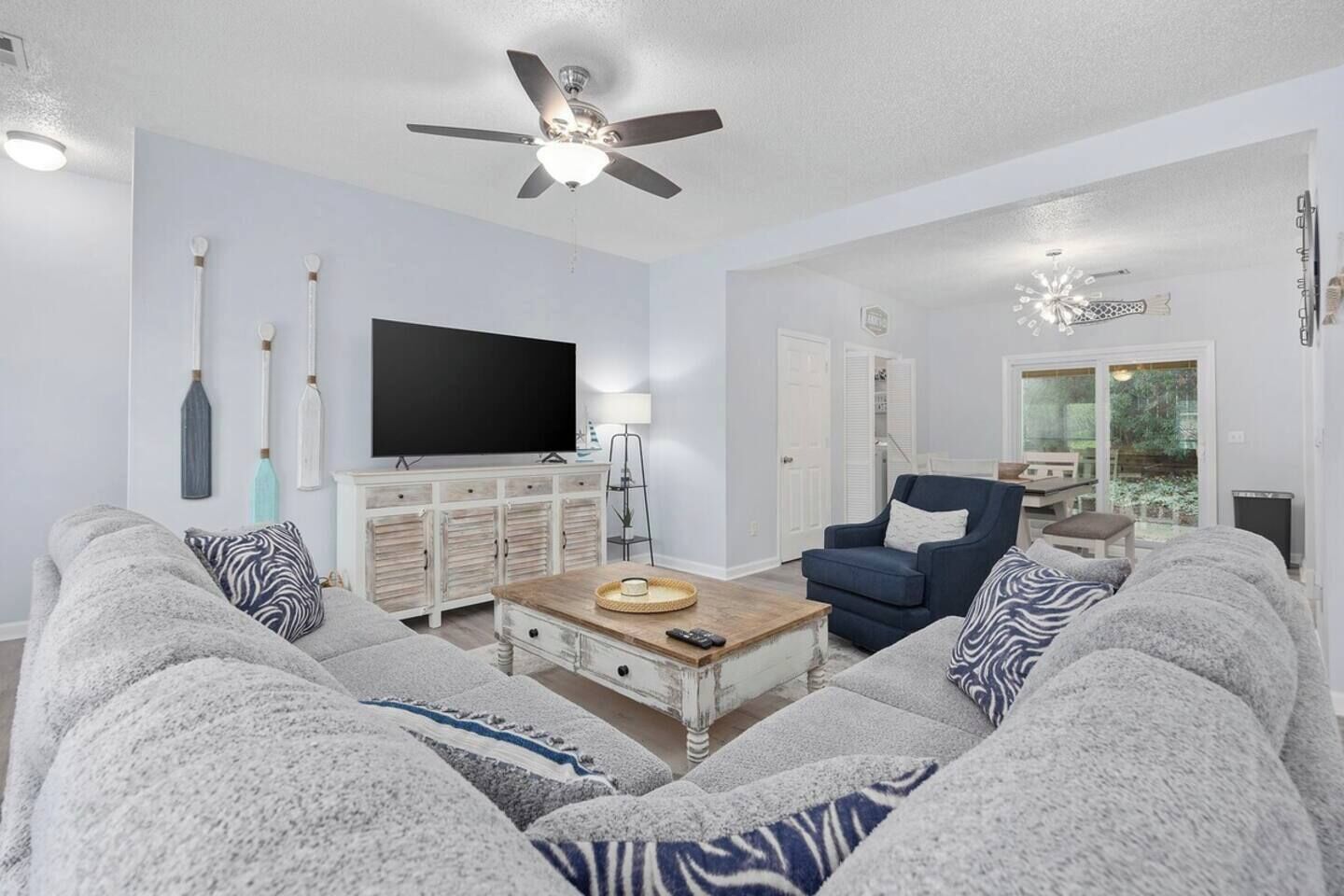 A living room with a sofa, armchair, coffee table, TV, and ceiling fan.